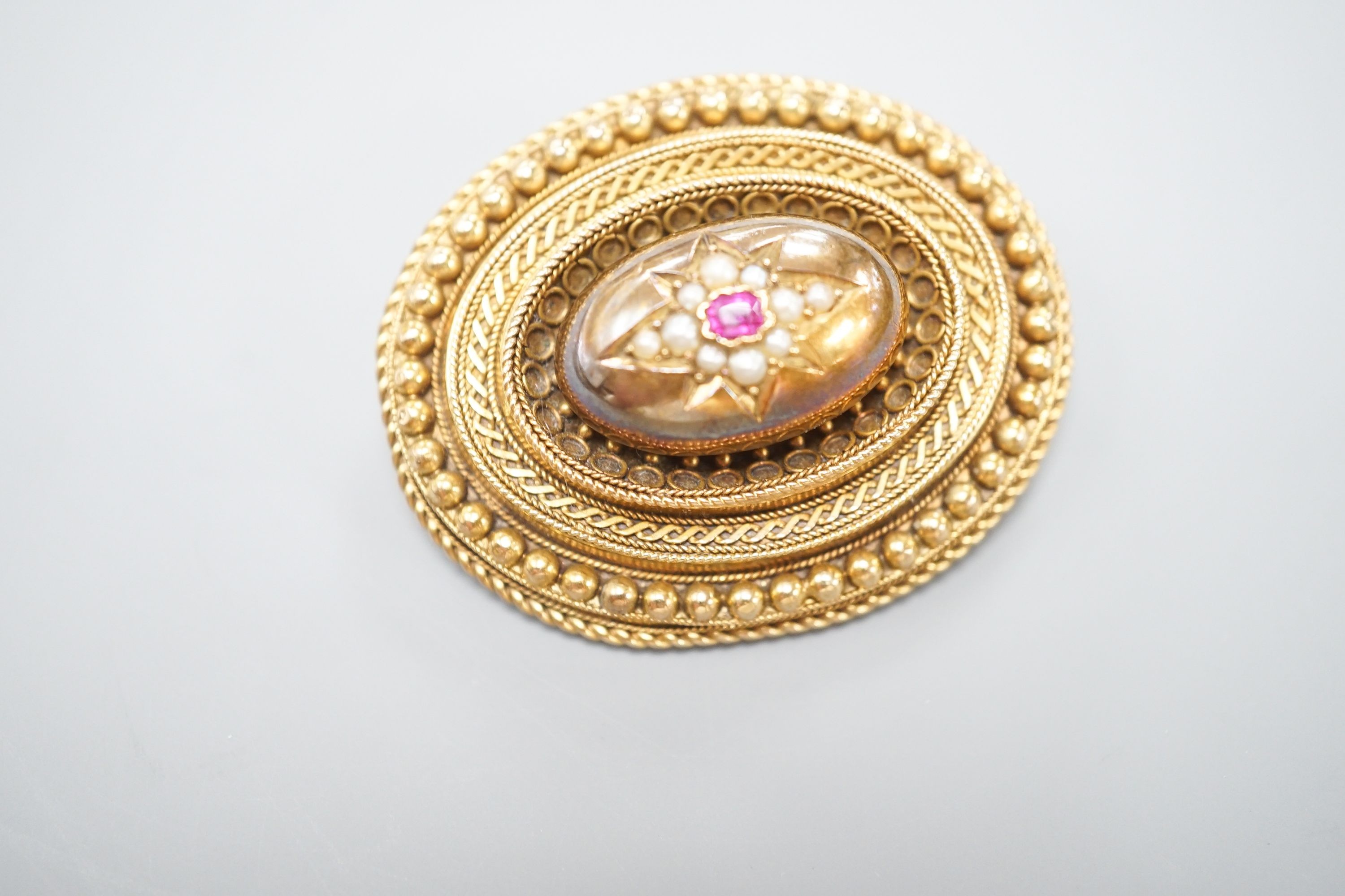 A Victorian yellow metal, ruby? and seed pearl set oval brooch, with glazed back, 43mm, gross weight 18.7 grams.
